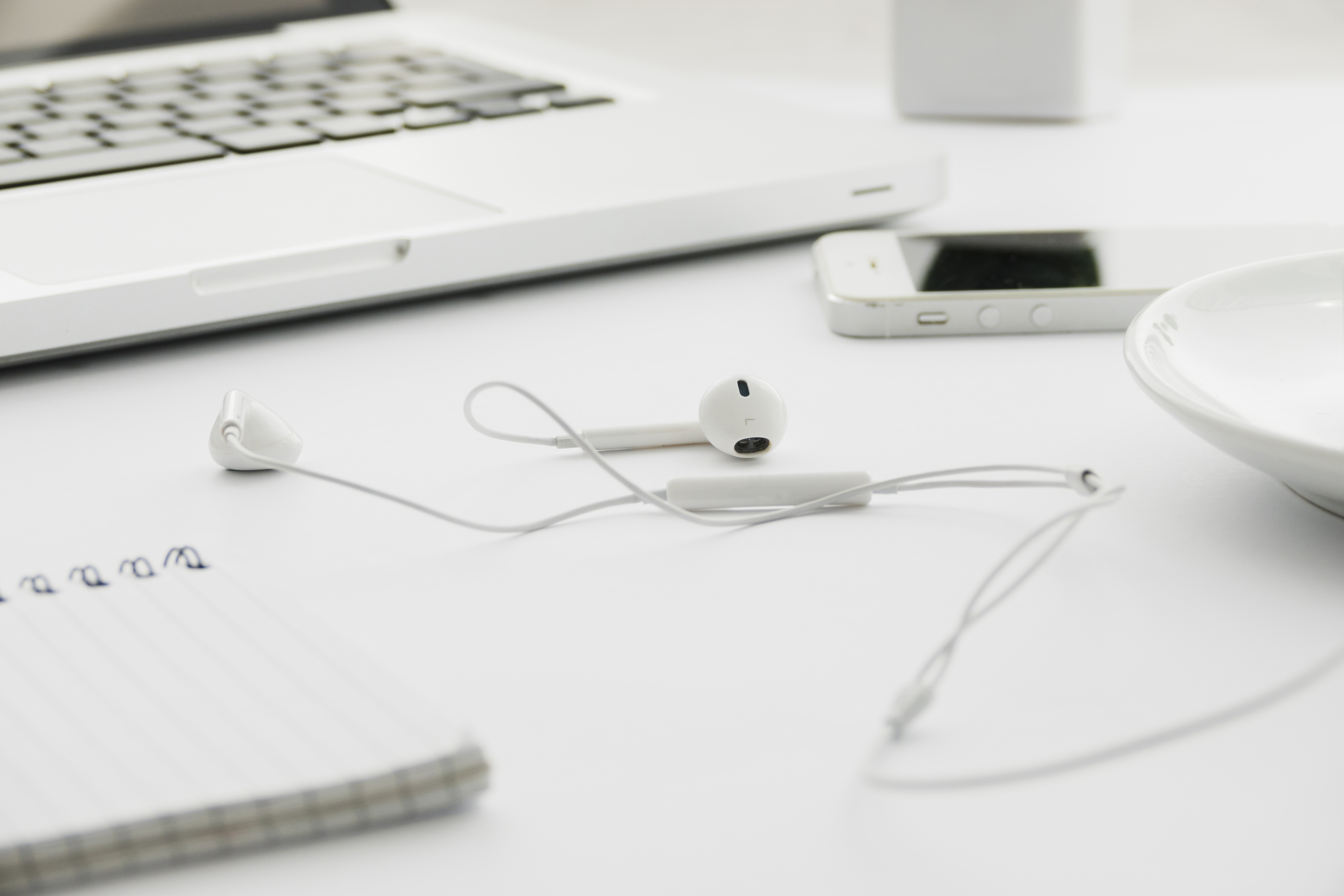 White desk with laptop, earbuds, smartphone and notebook — a minimal personal workspace